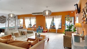 A spacious living area with a sofa set, a coffee table, and a wicker chair. There is a television mounted on the wall and a potted plant on a side table. - Novochoro Apartments (Albufeira)