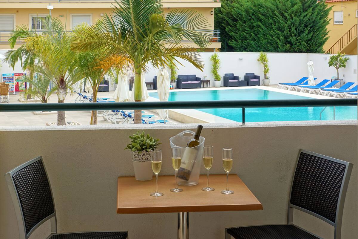 A balcony with a pool view, a table with wine glasses, and lounge chairs.
