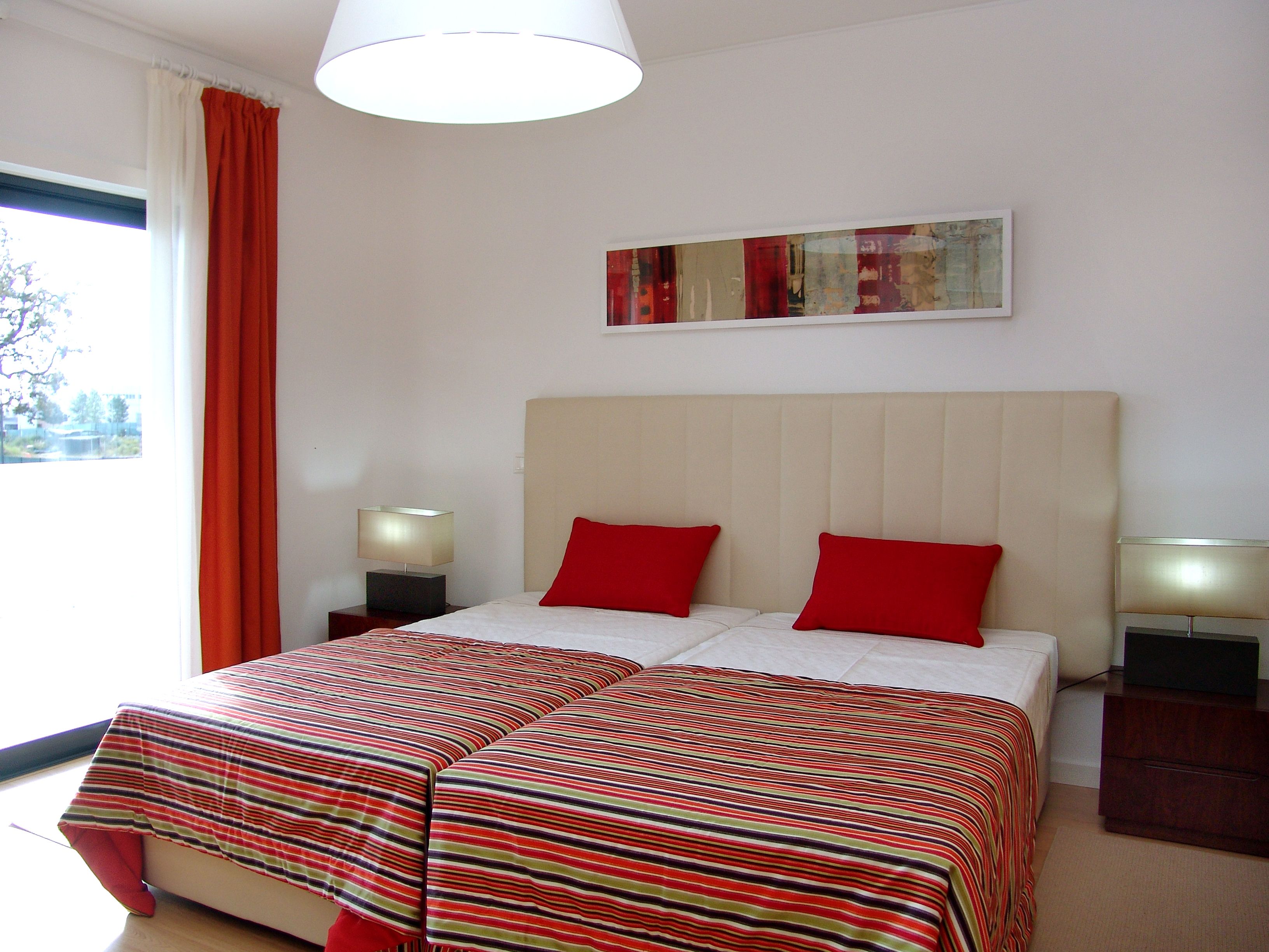 Ein Hotelzimmer mit einem Bett, zwei Nachttischen, einer Lampe, einem Fenster mit Vorhängen und einem Bild an der Wand.