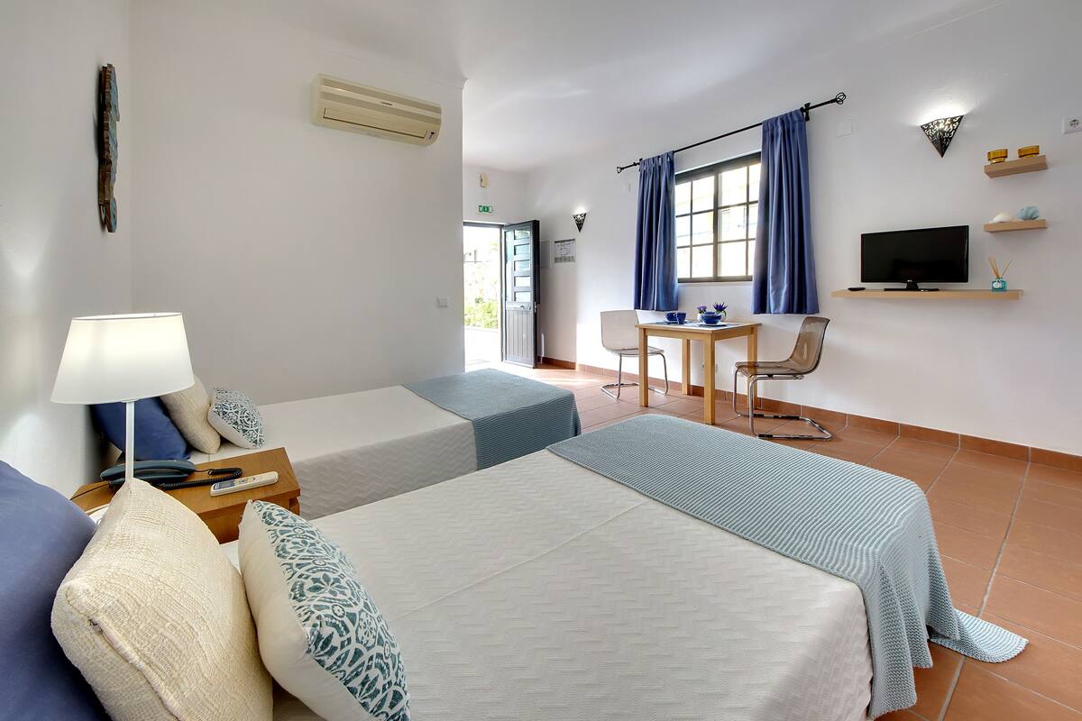 A hotel room with two beds, a desk, a chair, a TV, and a window with curtains.