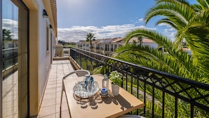 A balcony with a table set for dining, a railing, and a view of neighboring buildings and palm trees. - Novochoro Apartments (Albufeira)