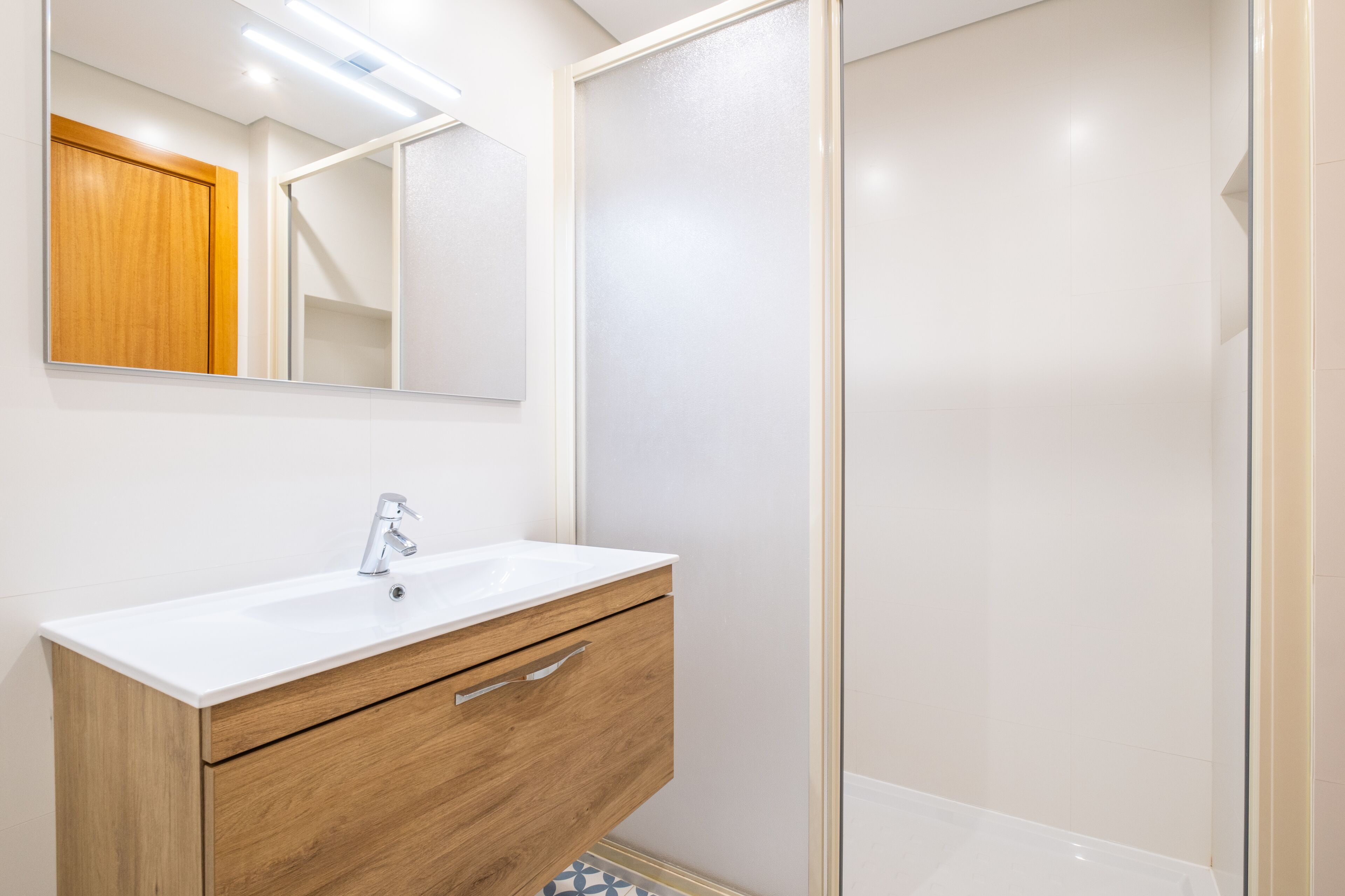 A bathroom with a white sink, wooden vanity, and a glass shower enclosure.