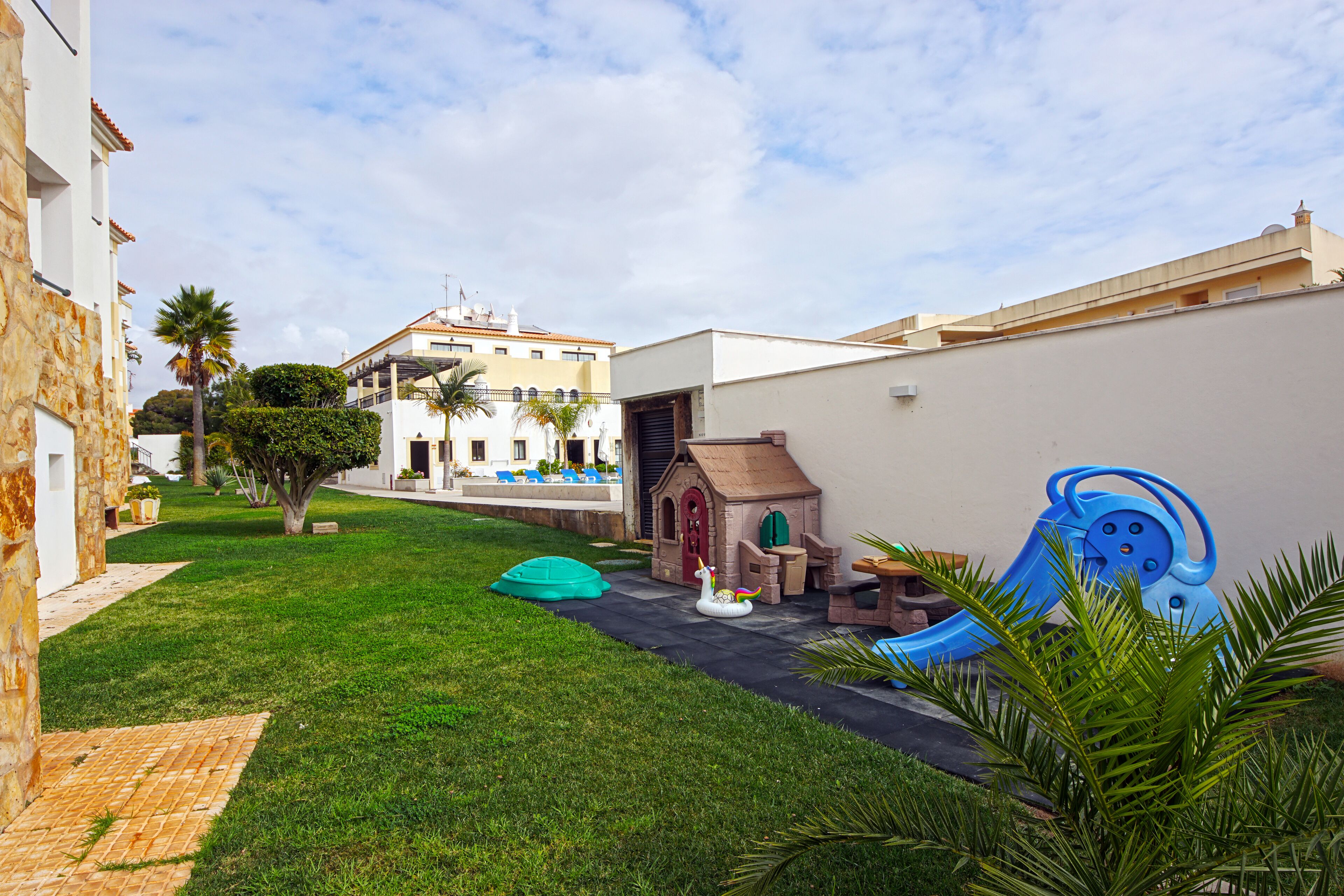 A courtyard with a play area, a small house, and a building in the background.