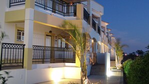 A multi-story hotel with balconies, a palm tree, and a well-lit entrance. - Novochoro Apartments (Albufeira)