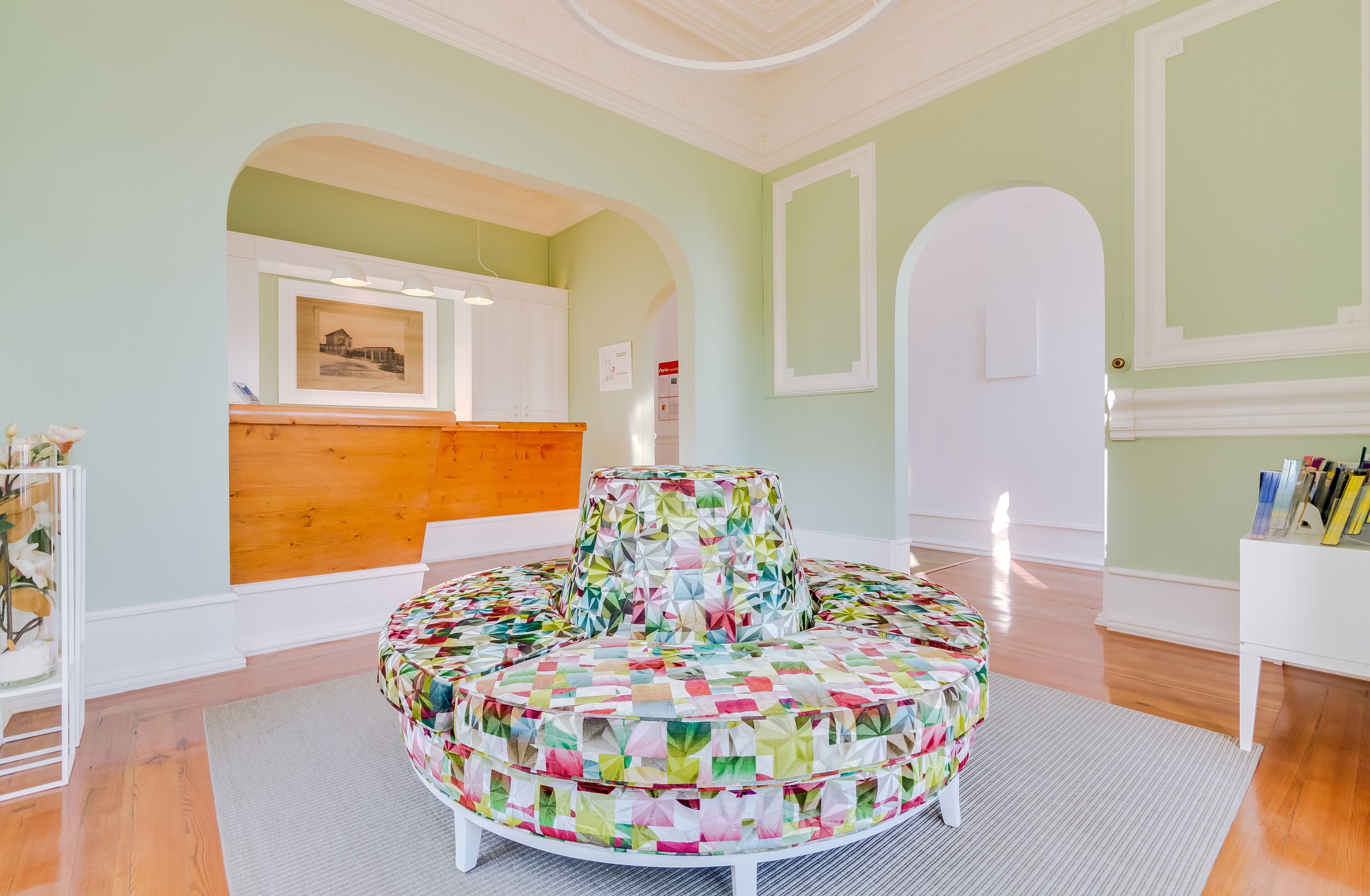 A circular seating area with a colorful geometric pattern, a reception desk with a framed picture, and a white door.