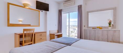 Habitación de hotel con dos camas, un escritorio, una silla, un televisor y un amplio ventanal con cortinas.