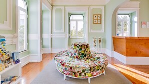 A spacious room with a round, colorful ottoman, large windows, and a wooden bench. - Hotel Vila Recife (Albufeira)