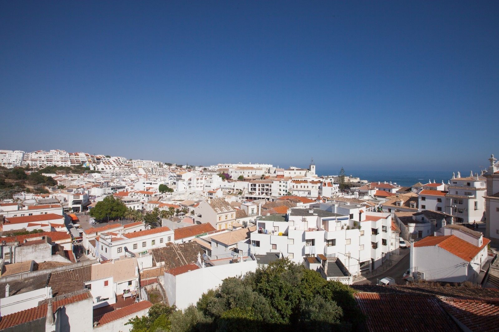 A coastal town with white buildings and red-tiled roofs, featuring a clear view of the sea.