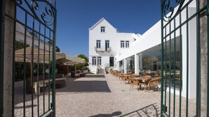 A courtyard with outdoor seating, a white building with a balcony, and a clear sky. - Hotel Vila Recife (Albufeira)