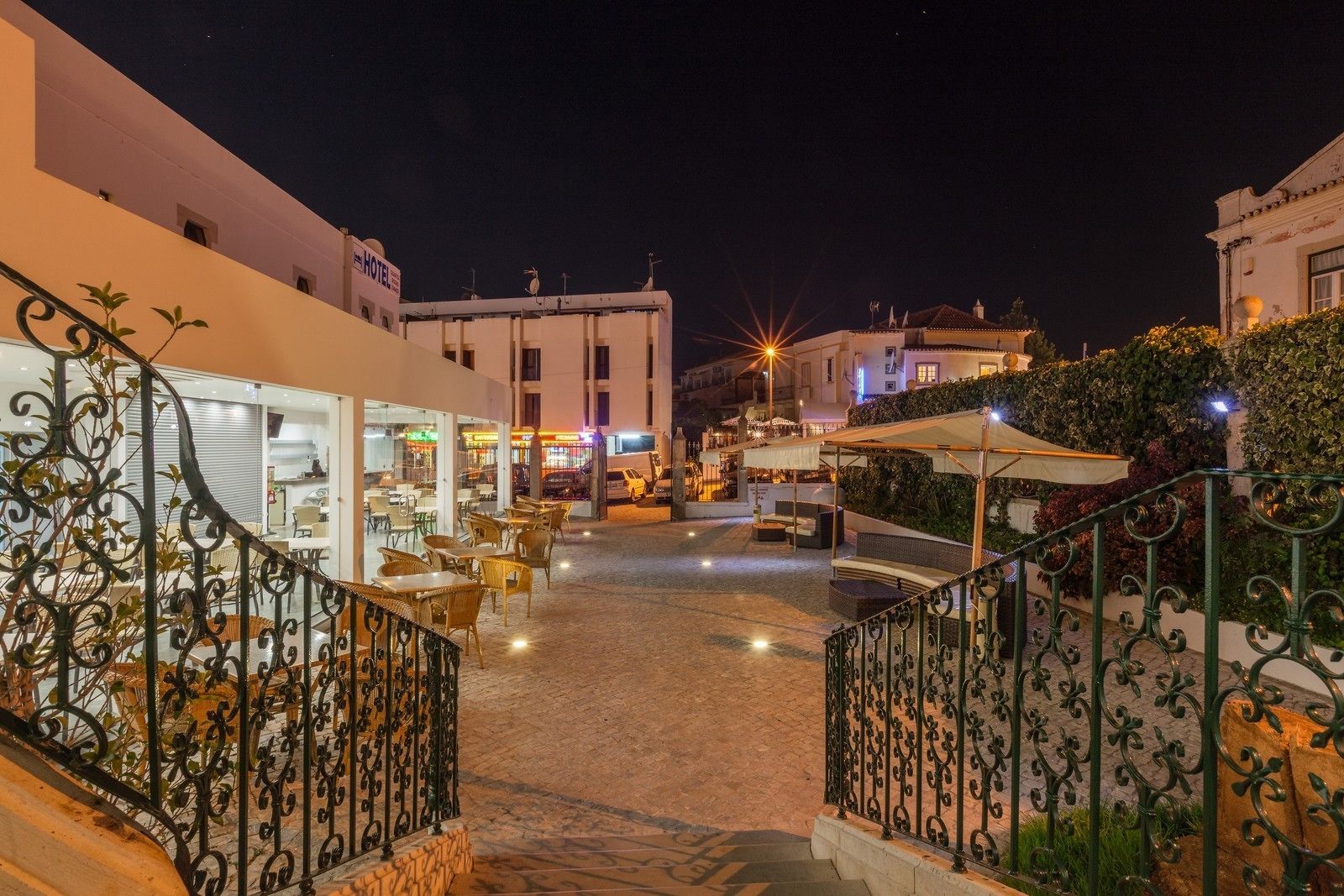 Vista nocturna de un patio de hotel con asientos al aire libre, una escalera y edificios circundantes.