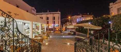 Vista nocturna de un patio de hotel con asientos al aire libre, una escalera y edificios circundantes.