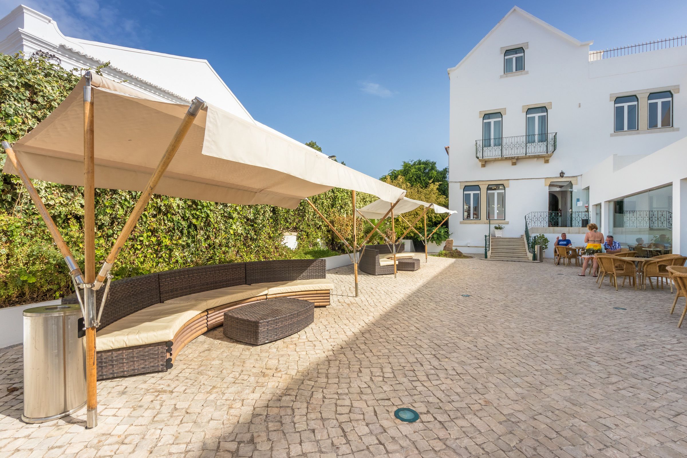 A courtyard with outdoor seating, a white building with balconies, and a paved walkway.