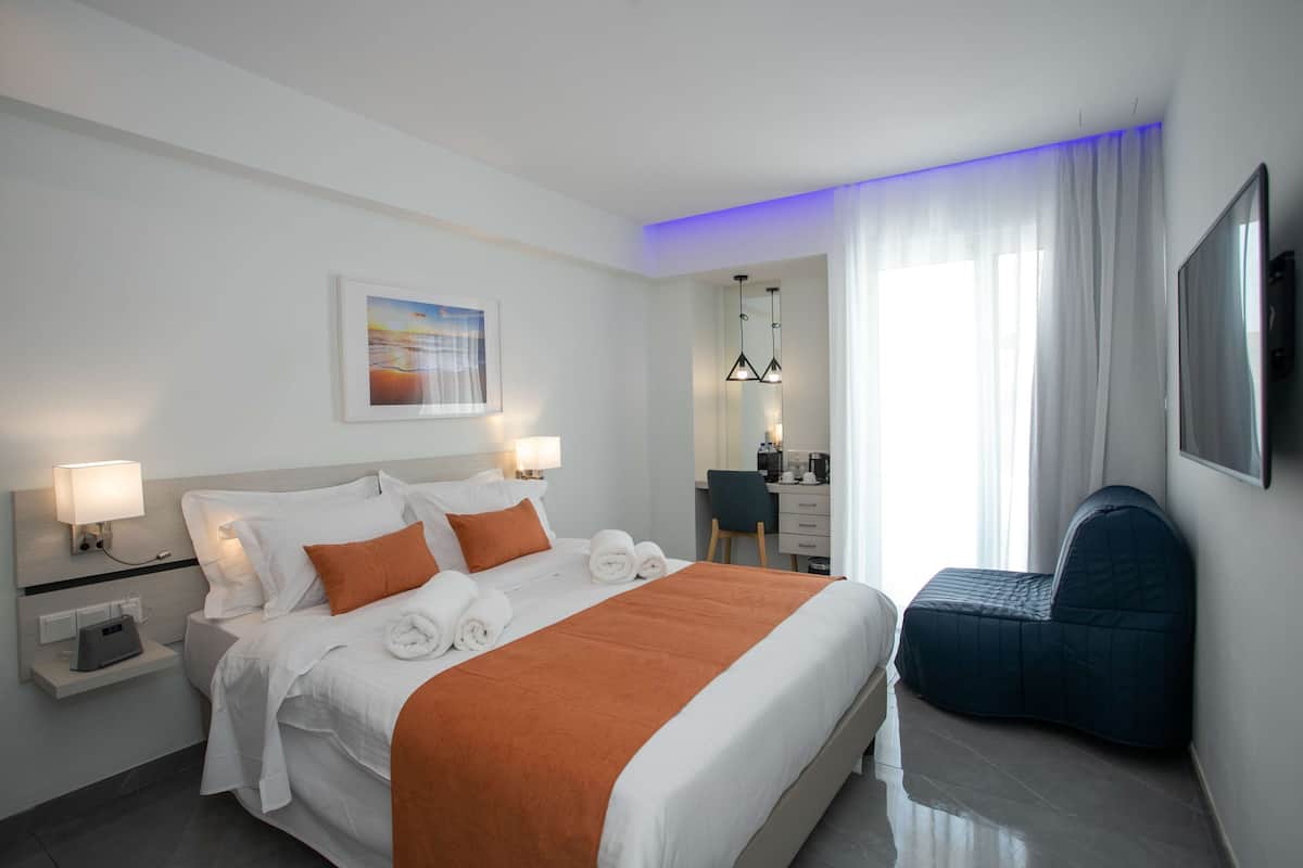 Ein Hotelzimmer mit Bett, Nachttisch, Lampe, Schreibtisch, Stuhl und einem großen Fenster mit Vorhängen.