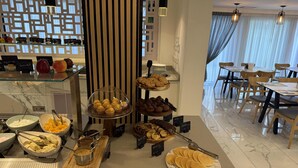 A breakfast buffet with various food items, a seating area with tables and chairs, and a decorative wall with vertical slats. - Best Western Plus Larco Hotel (Larnaca)