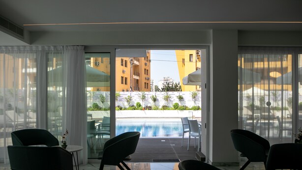 A modern hotel room with a glass door leading to a pool area, featuring a view of surrounding buildings and a landscaped garden. - Best Western Plus Larco Hotel (Larnaca)