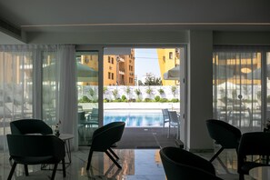 A modern hotel room with a glass door leading to a pool area, featuring a view of surrounding buildings and a landscaped garden. - Best Western Plus Larco Hotel (Larnaca)