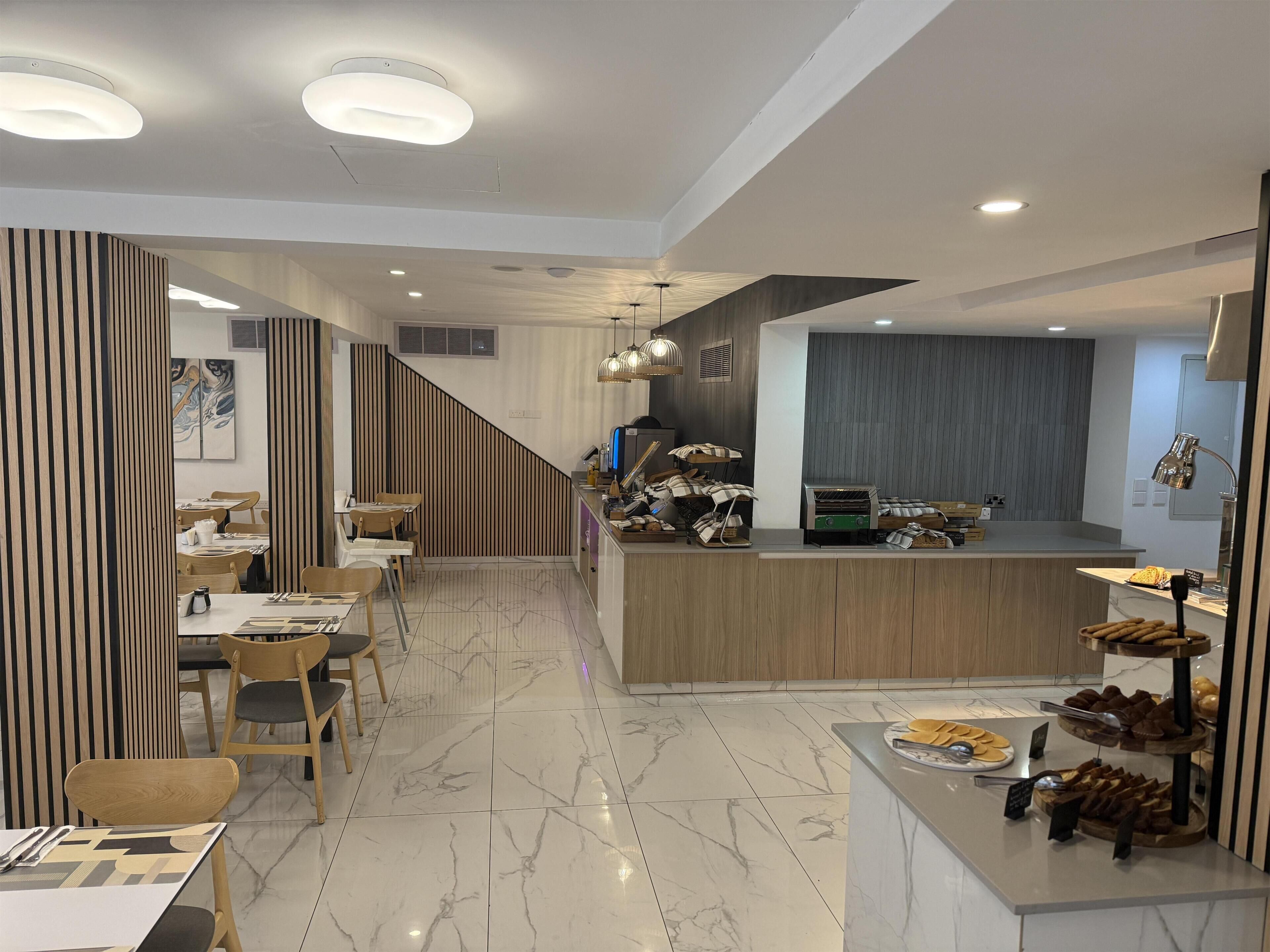 A modern restaurant with a central counter, wooden paneling, and a marble floor.