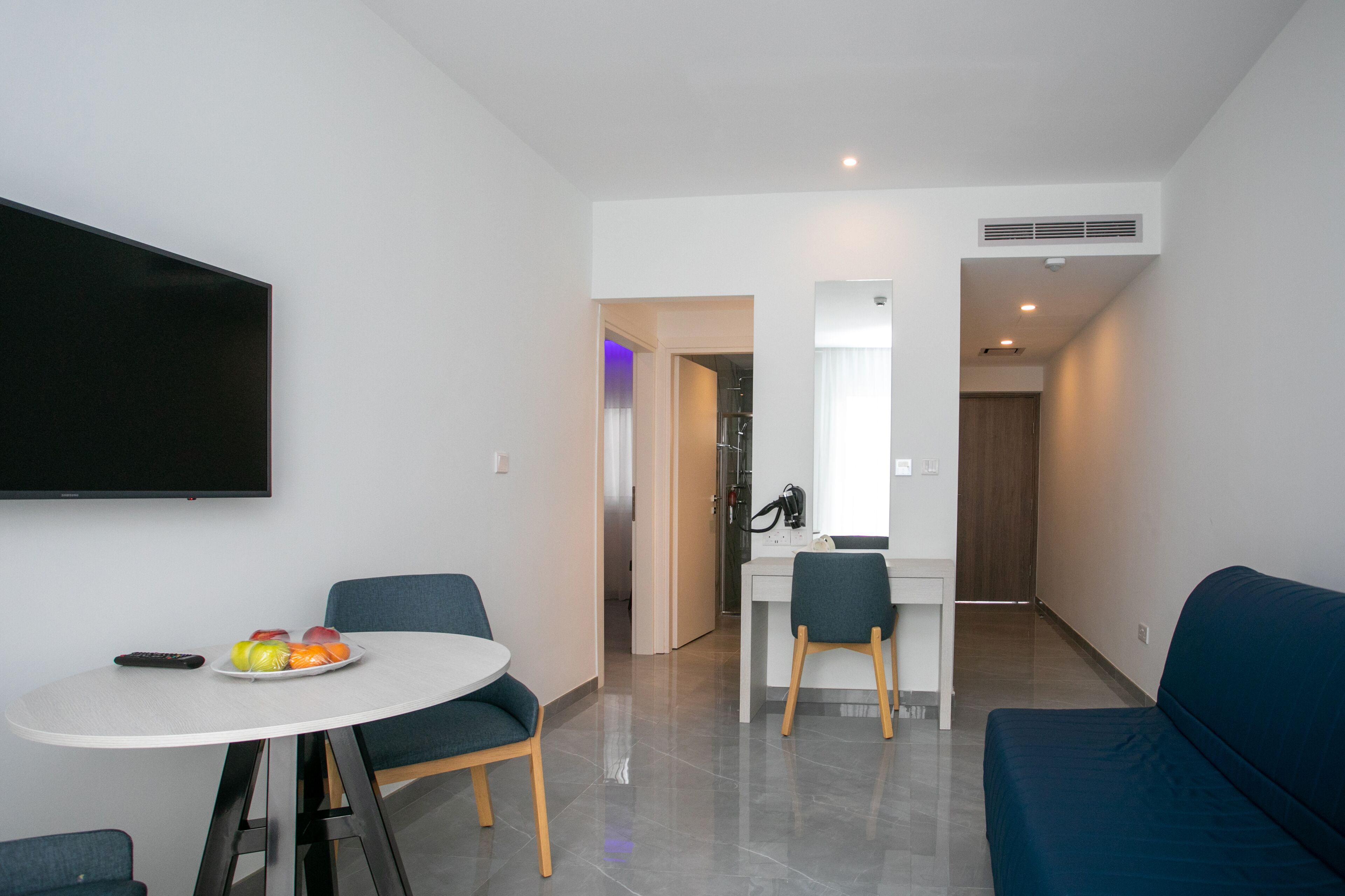 Una sala de estar moderna con un televisor de pantalla plana, una mesa de comedor con sillas y un sofá azul.