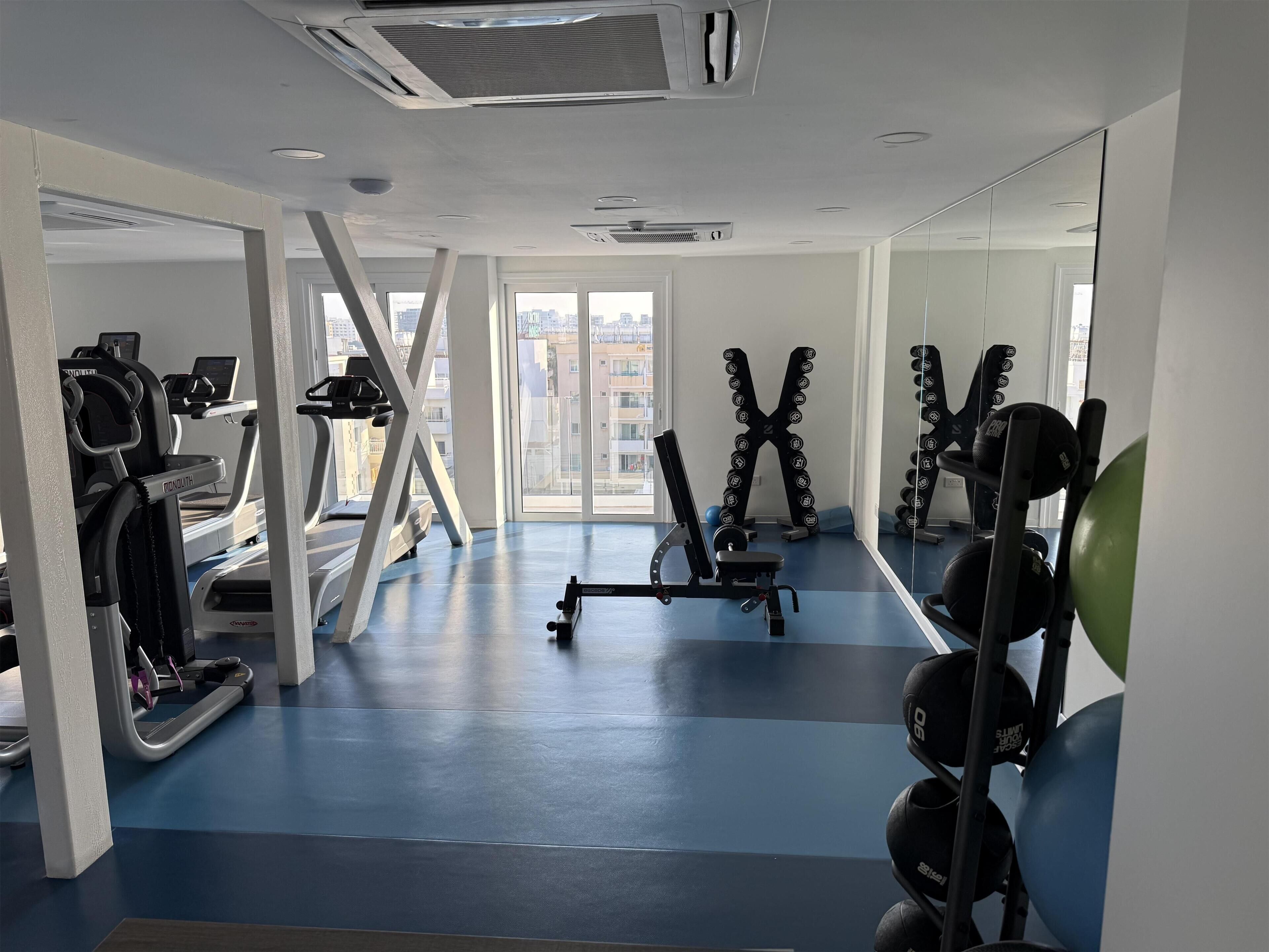 Un gimnasio con cintas de correr, máquinas de pesas y un espejo grande.
