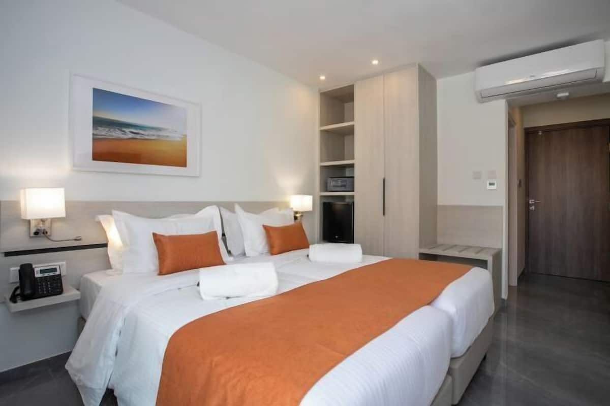 Ein Hotelzimmer mit Bett, Nachttischlampen, einem Gemälde, einem Kleiderschrank und einer Tür.