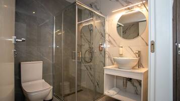 A modern bathroom with a glass-enclosed shower, a white toilet, and a marble-tiled vanity with a sink and mirror.