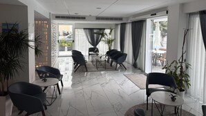 A modern hotel room with a large sliding glass door, a dining area with round tables and chairs, and a large potted plant. - Best Western Plus Larco Hotel (Larnaca)