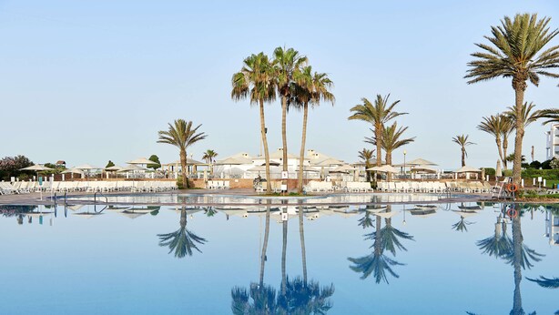 A pool with palm trees and umbrellas, reflecting in the water. - Iberostar Waves Founty Beach -All Inclusive (Agadir)