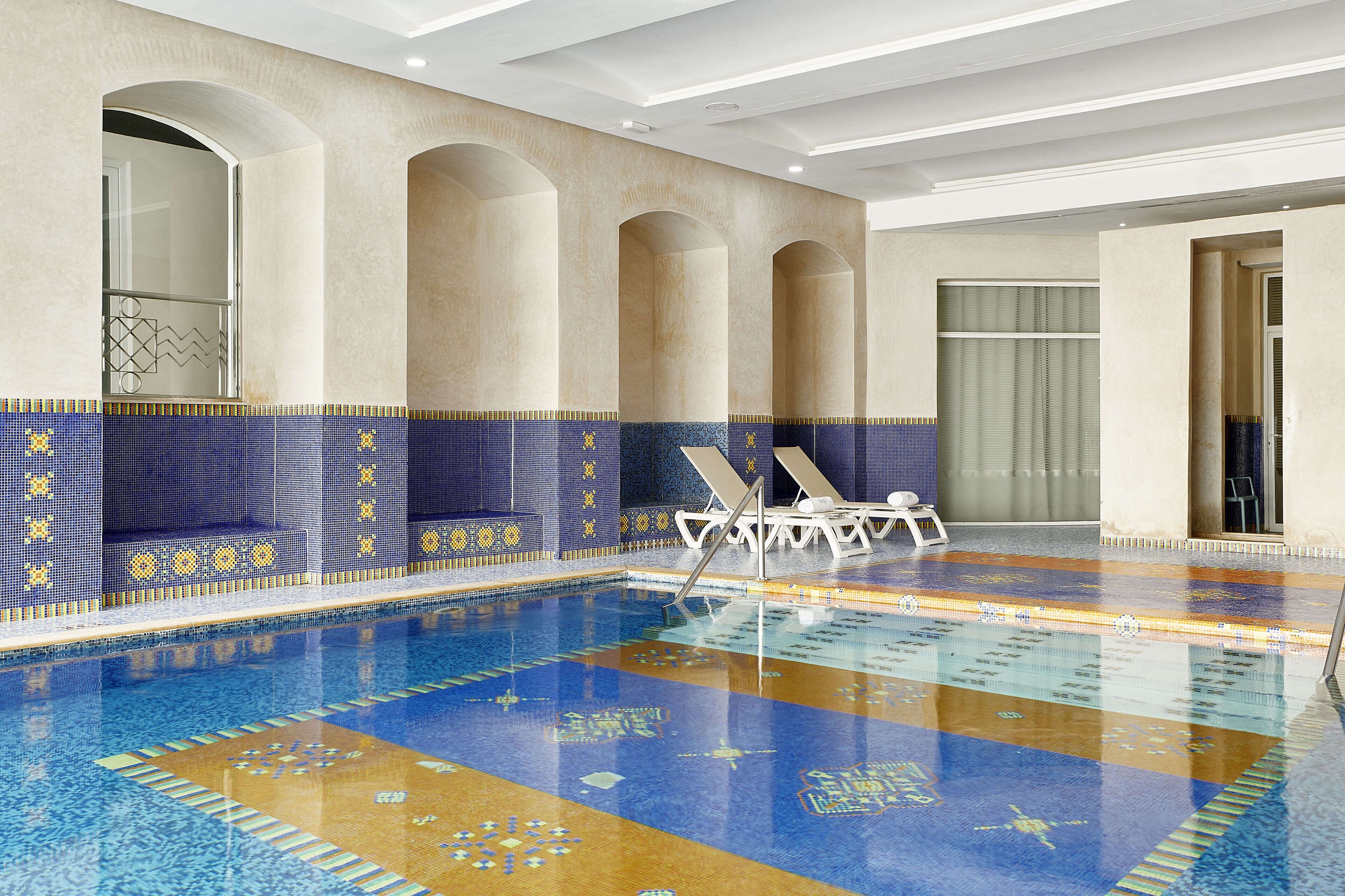 Una piscina con suelo y paredes de azulejos, sillas de descanso y una entrada con puerta de vidrio.