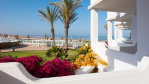 A balcony with white walls, a view of the beach, and colorful flowers. - Iberostar Waves Founty Beach -All Inclusive (Agadir)