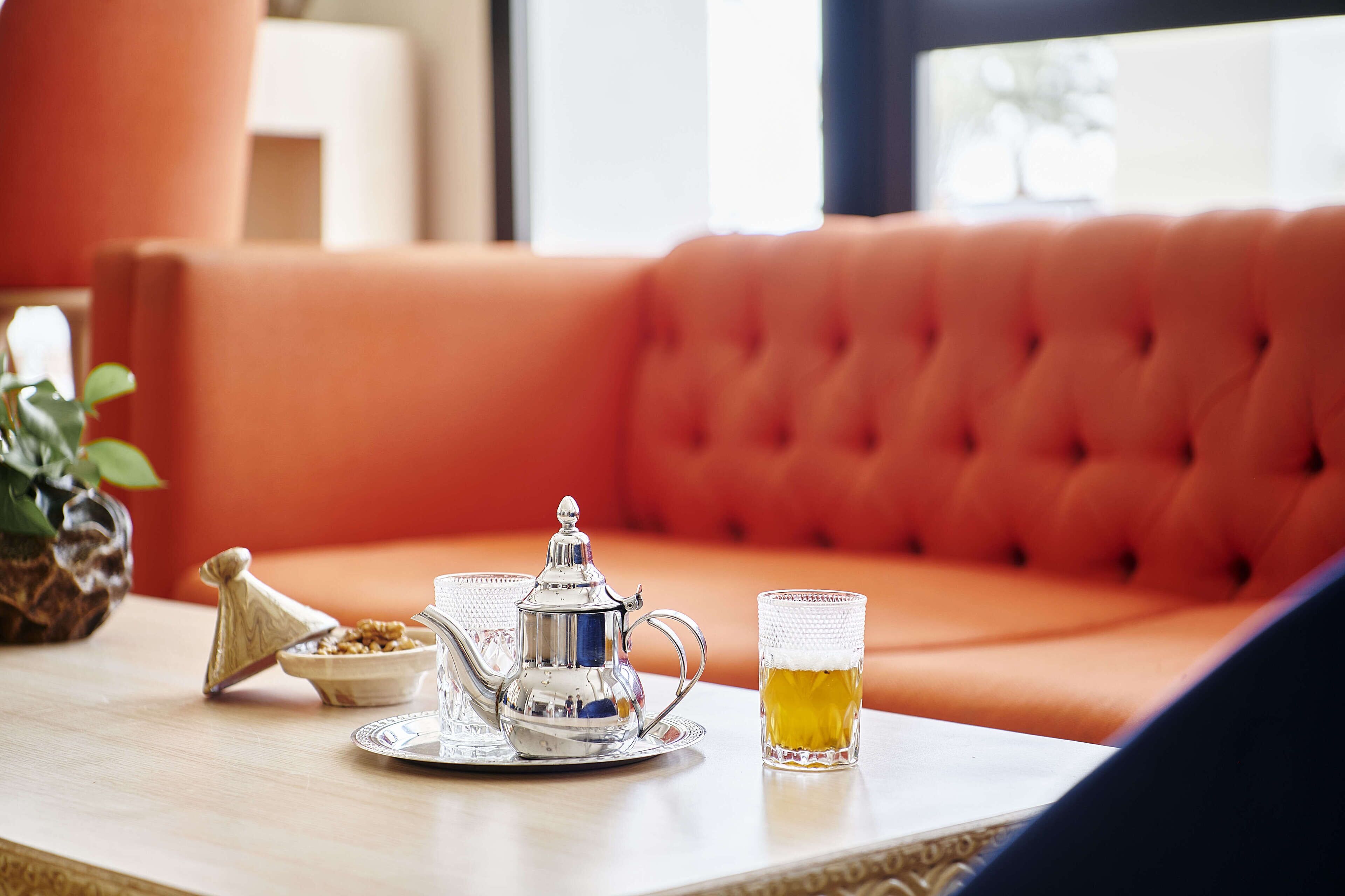 A table with a silver teapot, a glass of beer, and a bowl of nuts.