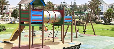 Un parque infantil con un tobogán, columpios y una estructura para escalar.
