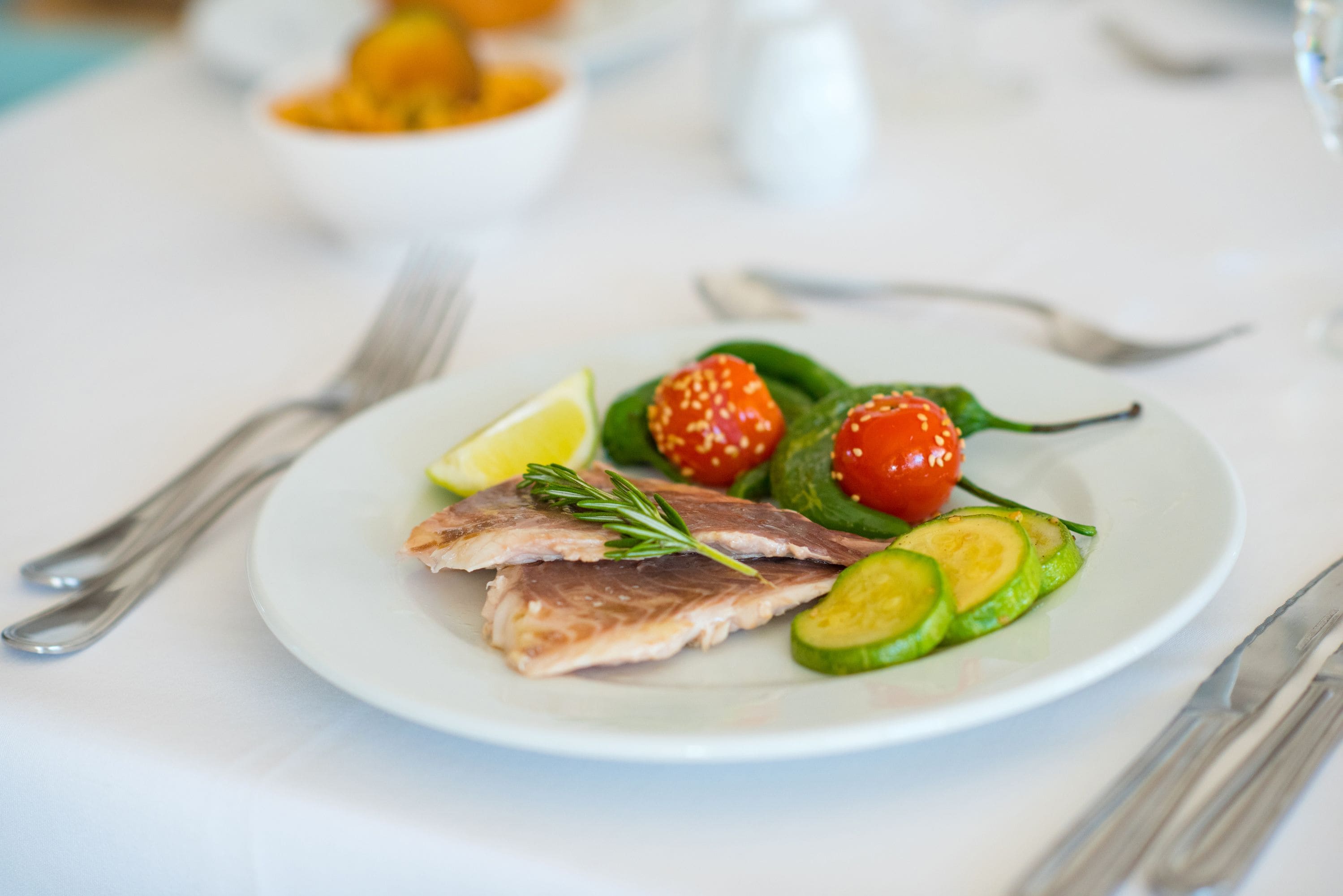 Une assiette blanche contenant des tranches de poisson, des tomates cerises, des rondelles de concombre et un quartier de citron.