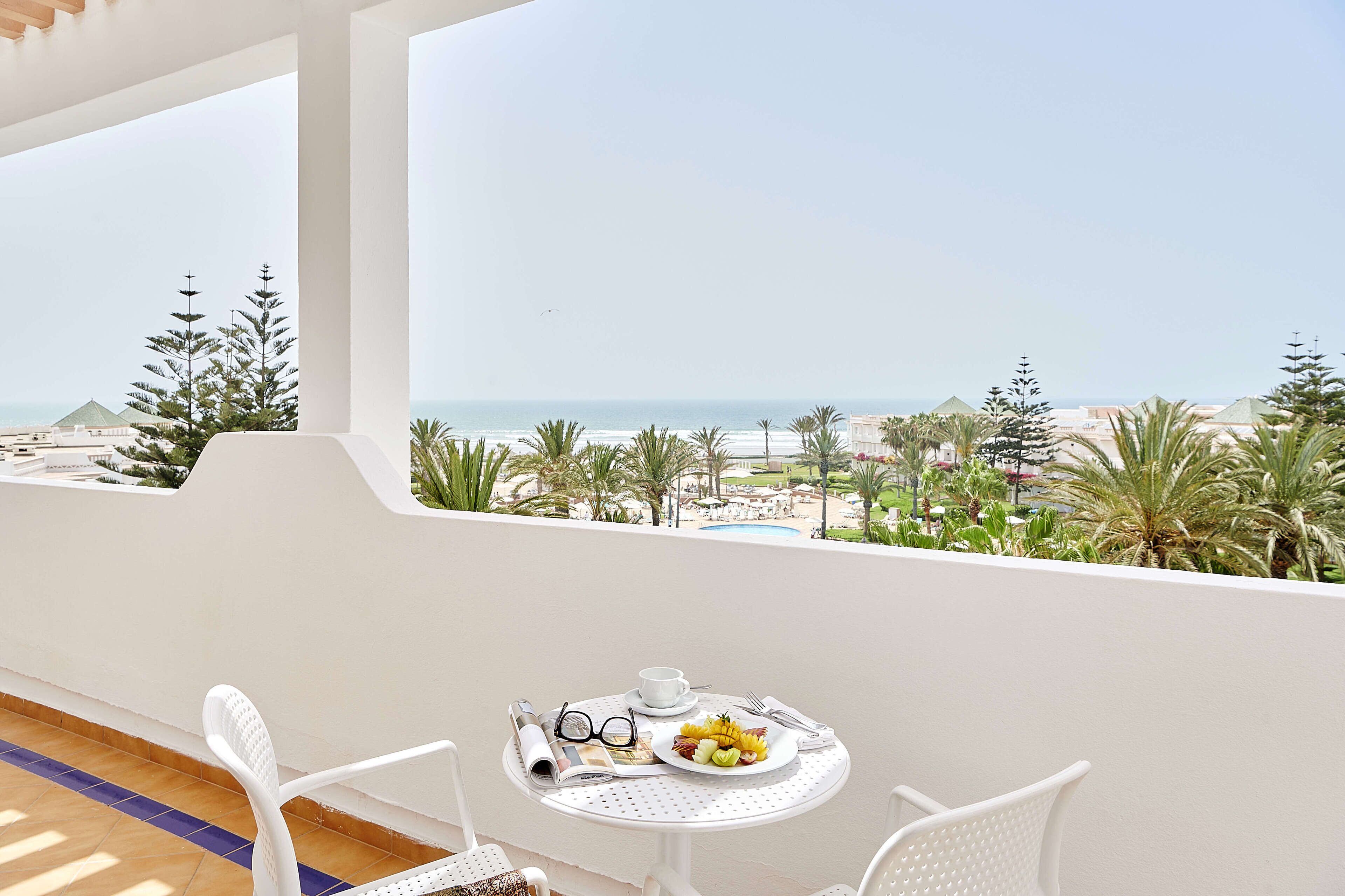 Een balkon met een ontbijttafel, met uitzicht op een strand en palmbomen.
