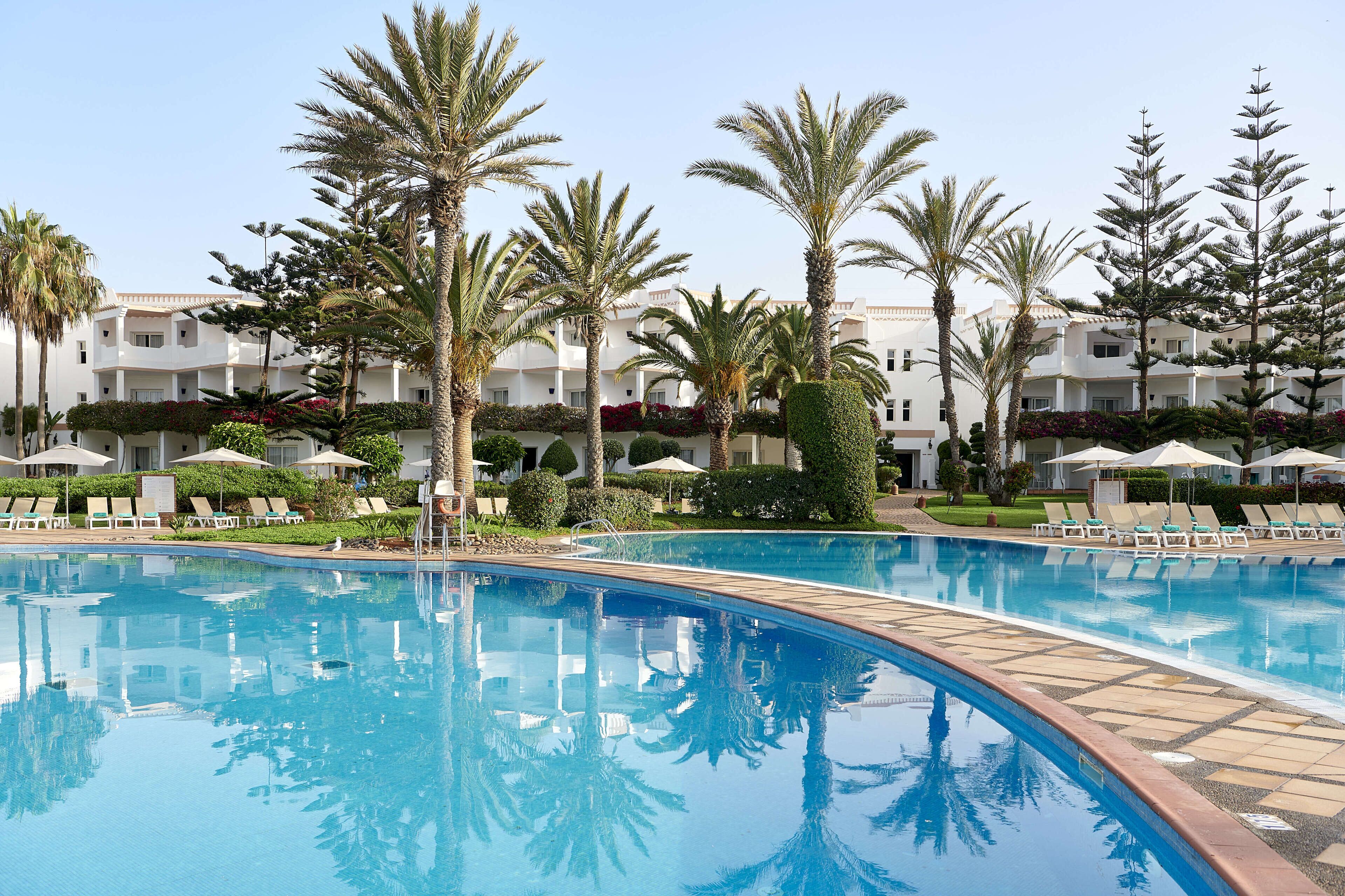 A swimming pool with lounge chairs and palm trees, surrounded by a building with balconies.
