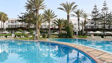 A swimming pool with lounge chairs and palm trees, surrounded by a building with balconies.