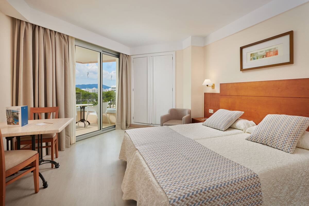 Ein Hotelzimmer mit einem großen Bett, einem Schreibtisch, einem Stuhl und Blick ins Freie.