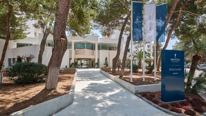 Une entrée d’hôtel moderne, avec un chemin menant au bâtiment, entouré d’arbres et agrémenté d’un jardin paysager.