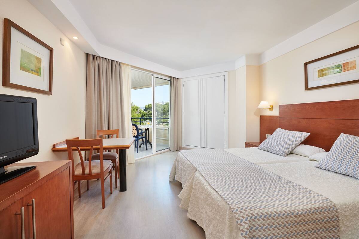 Ein Hotelzimmer mit Bett, Schreibtisch, Stuhl, Fernseher und Blick ins Freie.