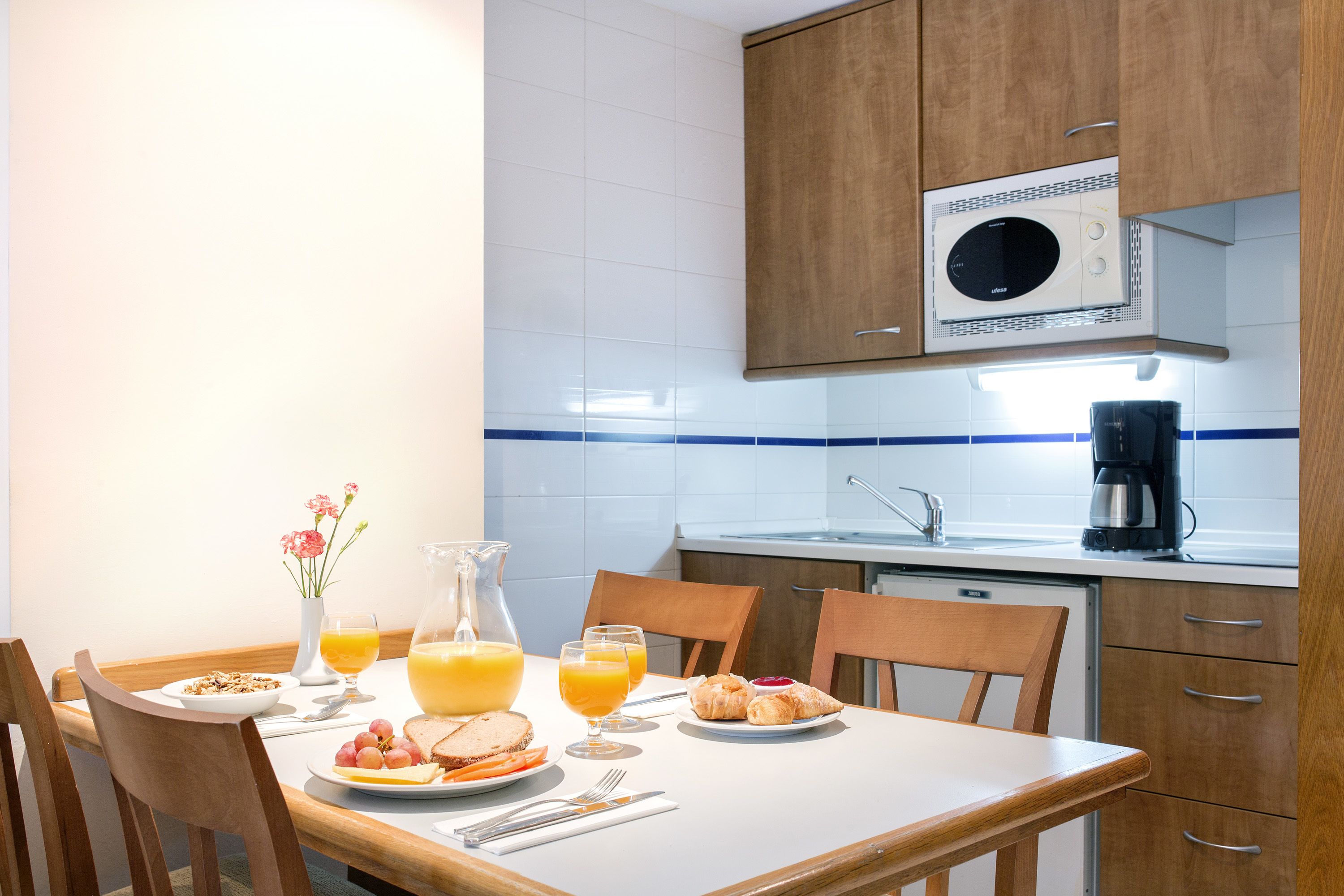 A breakfast setup with a table, chairs, and a kitchen area with a coffee maker and microwave.