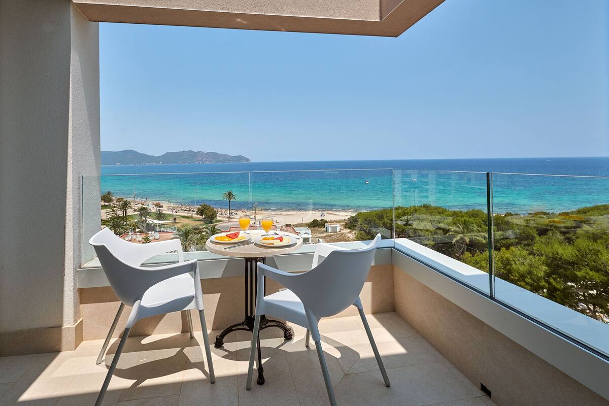 Ein Balkon mit Tisch und Stühlen mit Blick auf Strand und Meer.