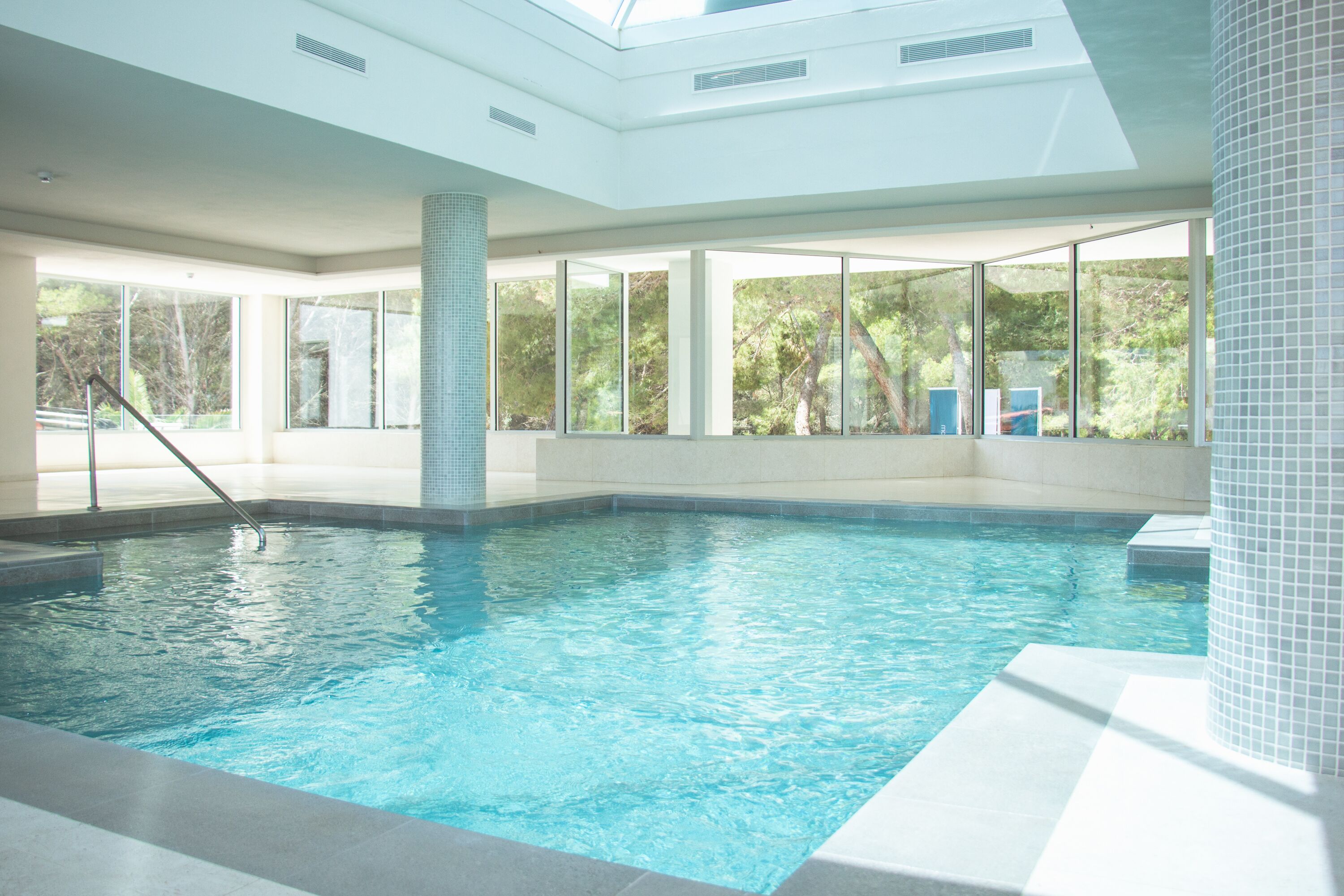 An indoor swimming pool with clear glass walls, a tiled floor, and a metal ladder.