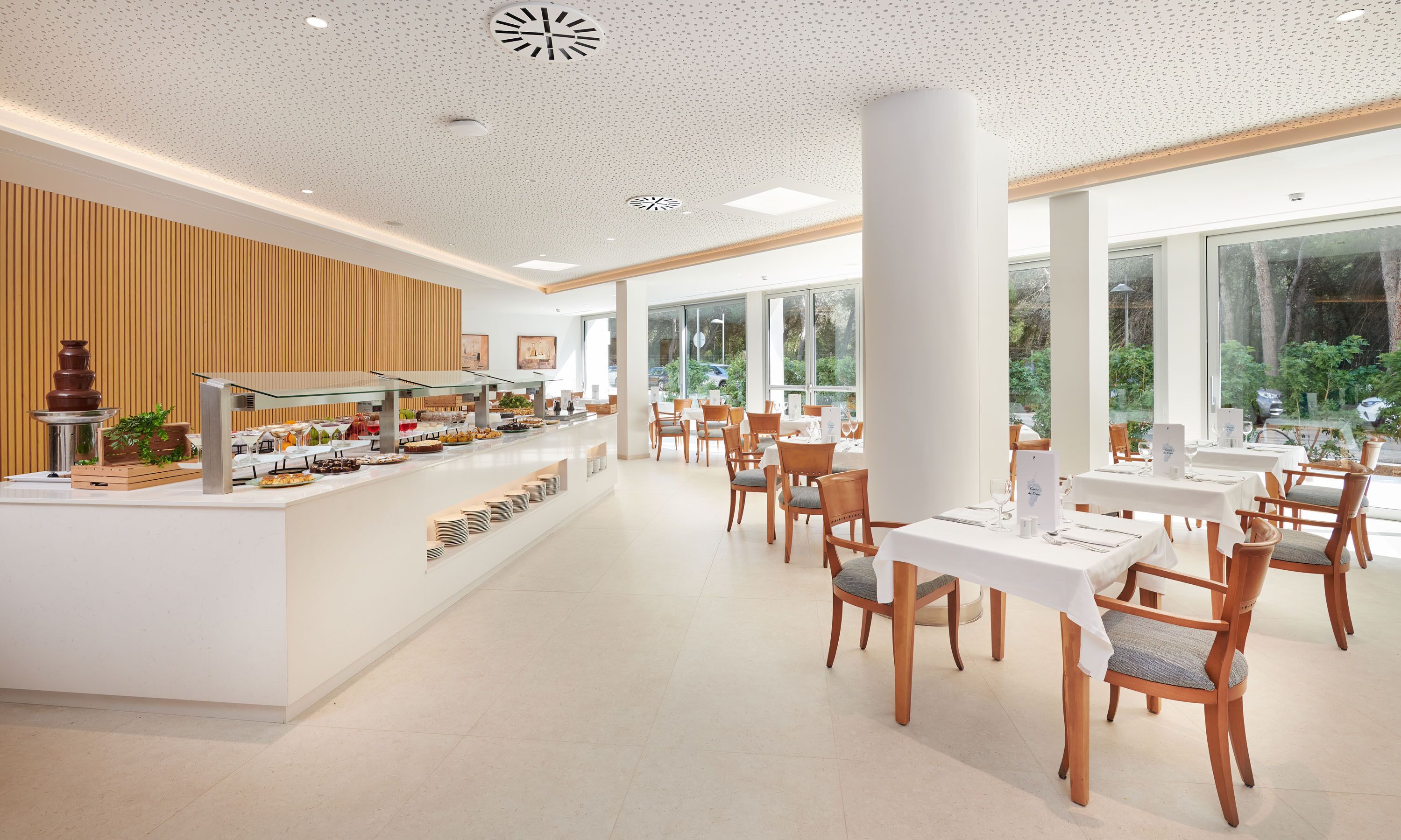 A modern dining area with a buffet, wooden paneling, and large windows offering a view of the outdoors.
