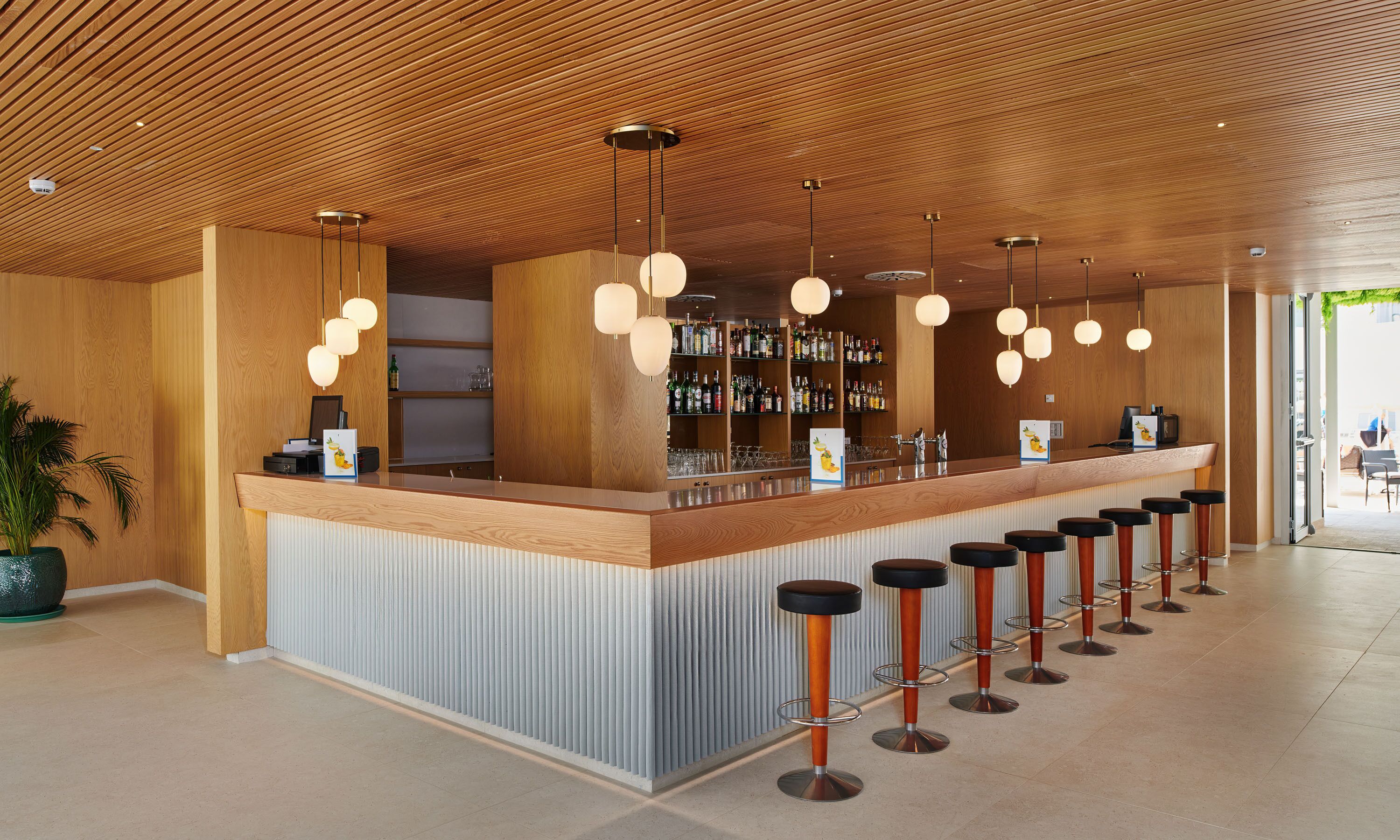 A modern bar area with wooden ceiling, bar stools, and pendant lighting.
