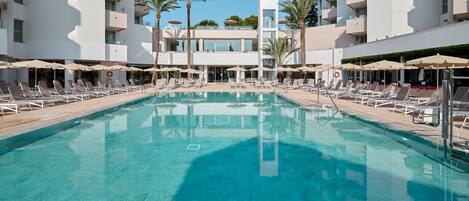 A swimming pool with lounge chairs and umbrellas, surrounded by a modern building with balconies.