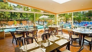 Un comedor interior con mesas y sillas, una piscina al fondo y amplias ventanas.