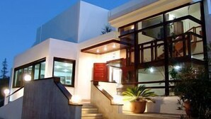 Una casa moderna de dos pisos con una escalera que conduce a la entrada, ventanas amplias y una planta en maceta en el porche.