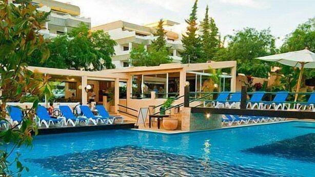 Una piscina con sillas de descanso y un área techada, rodeada de vegetación y edificios.