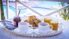 A breakfast tray with pastries, coffee, and orange juice, set on a table with a pool view. - Apartamentos Tisalaya Park (San Bartolome de Tirajana)