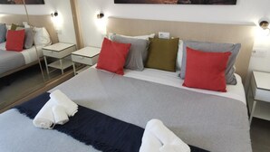 A hotel room with a large bed, two bedside tables, a nightstand, a mirror, and a painting of a sunset over the ocean. - Apartamentos Tisalaya Park (San Bartolome de Tirajana)