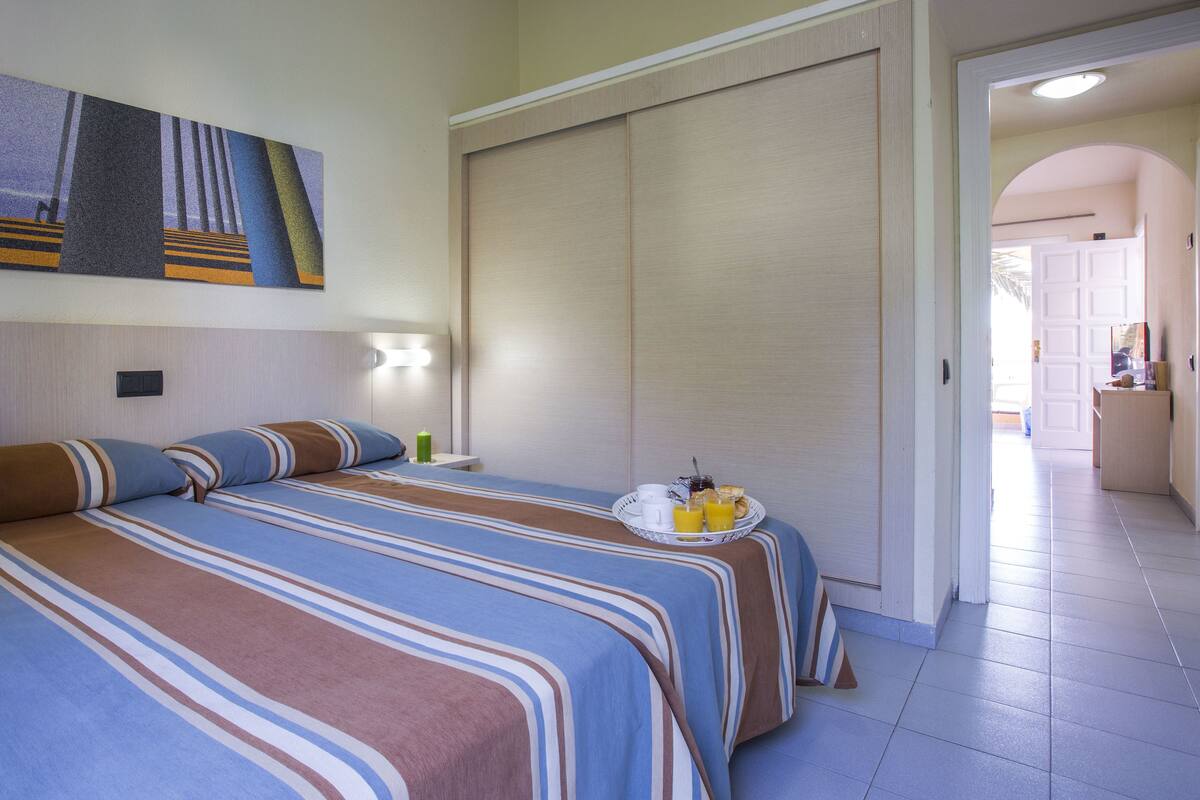 A hotel room with two beds, a painting on the wall, a nightstand with a lamp, and a breakfast tray on the side table.